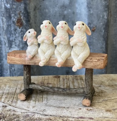 Kaniner som sitter på rad på en bänk. Söta vita kaniner med långa öron. Bänken dom sitter på ser ut att vara av trä vilket ger e