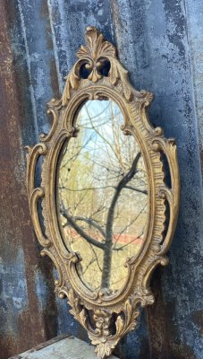 Vacker spegel i guld. Oval i modellen med snirklig barock ram. Designad i en antik och gammeldags stil.  Modellen formen på speg