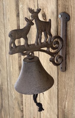 Vacker dörrklocka i järn gammeldags design i bruna nyanser med dekorerad med hjortar upptill och smides konsol mot väggen. Klock