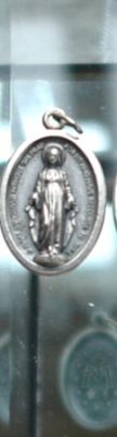 Franskt emblem/Krucifix i oval  modell med madonna , bild och text på två sidor olika. I silver färgad metall. Hänger i ståltråd