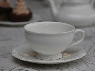 Vit Fransk Te kopp med fat i porslin. Detaljrik med vackert mönster runt om i det vita porslinet. Koppen står på en liten fot oc