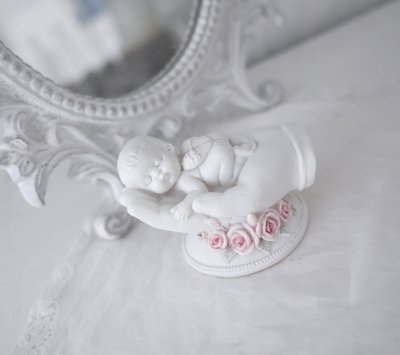 Vit ängel bebis som vilar i en öppen hand dekorerad med rosa rosor. En detalj full och välarbetad prydnad och minnes sak passand