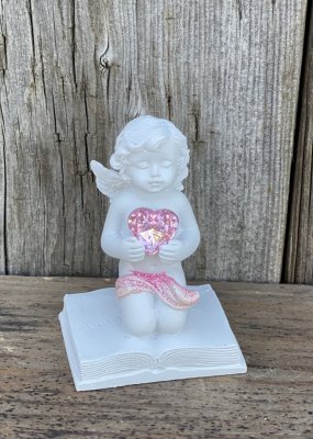 Söt vit ängel som står på knä på en bok med ett diamant liknande rosa hjärta i händerna. Detaljrik och välarbetad med söta detal