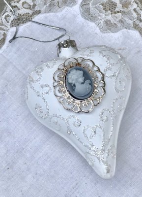 Vitt glashjärta / julgranskula i glas. Går i en vit nyans dekorerad med pärlor och gammeldags motiv . Hänger i vackert band uppt