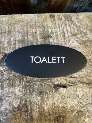Oval svart TOALETT skylt i plåt