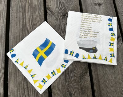 Student servetter med sångtext ”Sjung om studentens lyckliga dag” på en sida och svenska flaggan på andra sidan. (komposterba
