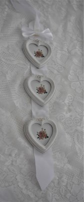 Fotorams kollage med tre stycken vita hjärtformade fotoramar. Fotoramarna sitter på ett brett vackert vitt tyg band med rosett.