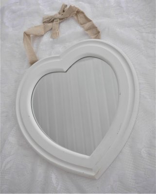 Vit hjärtformad vägg spegel i större modell. Spegeln har en bred vit lätt snidad ram runt om. Vit målad med fabriks skavda /slit