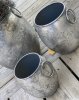 Kruka/urna/tunna med ledade handtag på sidorna. I rundad modell tillverkad i metall och går i en grå silver nyans mot antik sil