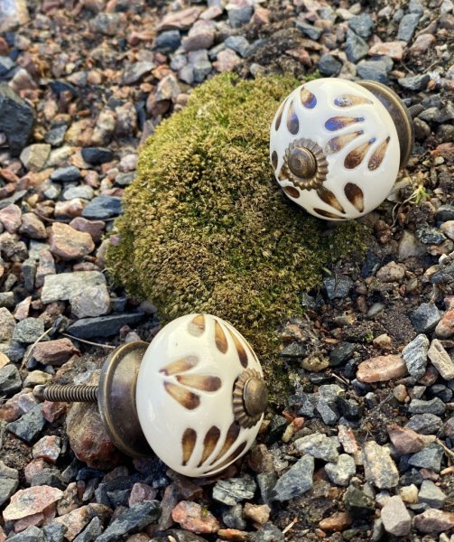 Rundad porslinsknopp med handmålat mönster i brunt, guld och vitt. Går i en orientalisk stil med utanpå liggande mönster. Välar