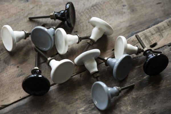 Cream vit keramik knopp med blank glaserad yta. Rund modell med diskret upphöjd kant runt om. Stomme i antik guld färgad nyans.
