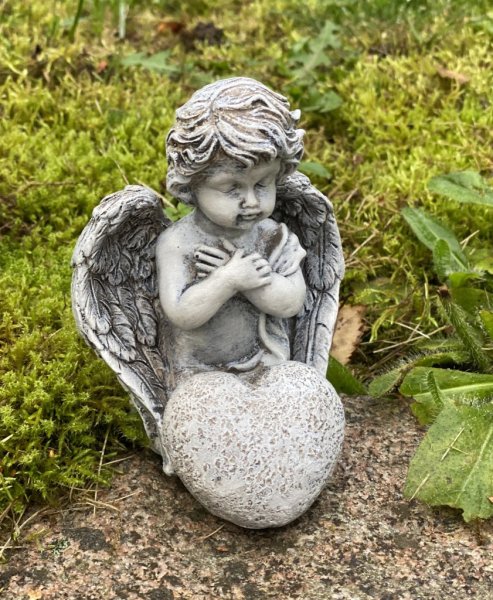 Bedjande ängel som sitter ner på knä, med hjärta och stora vingar. Går i en grå vit nyans som liknar sten. Detalj full och välar