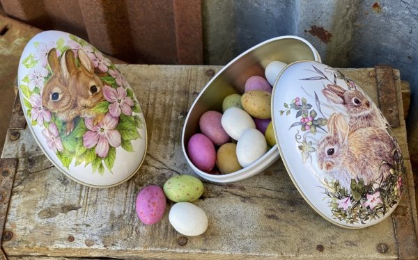 Påskägg /dekorations ägg i plåt. Med vackert motiv av kaniner omgivna av blommor på vit botten. Finns i två modeller -Mörkbruna