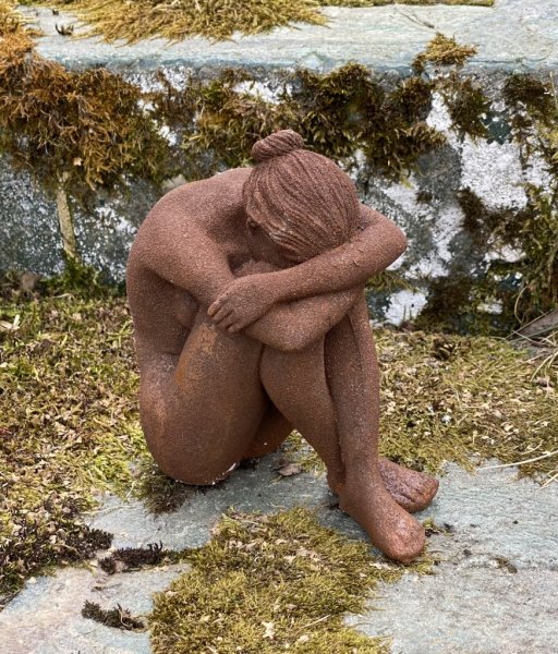 Aura rostig staty/figur av en kvinna i rost som sitter ihop kurad. Detaljrik och välarbetad. Ruffigt rostig modell. Höjd: ca 15