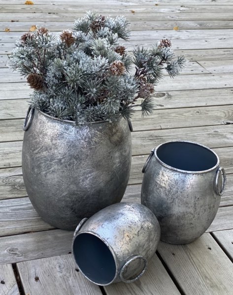 Kruka/urna/tunna med ledade handtag på sidorna. I rundad modell tillverkad i metall och går i en grå silver nyans mot antik sil
