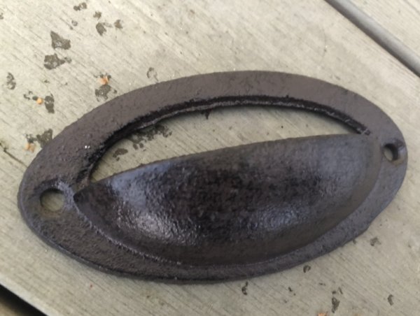 Gammeldags handtag i järn. Skålformat med två fäst punkter, går i en mörk brun ruffig nyans. . Att fästa med öppningen upp eller