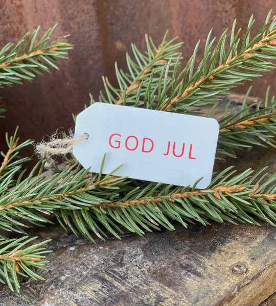 Liten vit God Jul skylt i trä. Med snöre upptill och text på en sida. Mäter 6,3cm utan snöre mätt