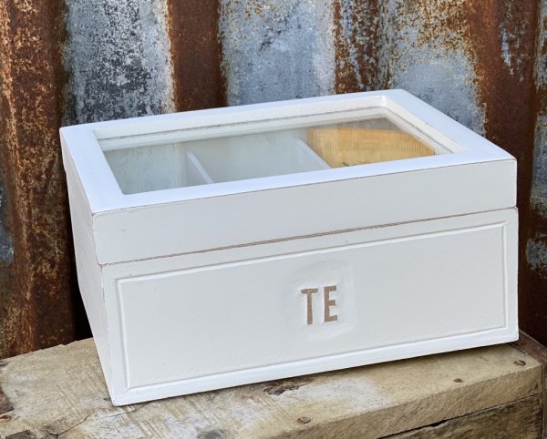 Vit trälåda med glaslock och text TE på två sidor. Fack inuti att dela upp te sorterna i. Lantlig stil med lätt fabriksnötta kan