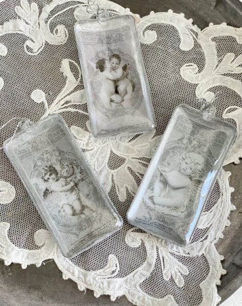 Julgranskula / dekorationskula i avlång modell med ängelmotiv. Finns i tre olika motiv -Pussande änglar -Ängel med blomsterkrans