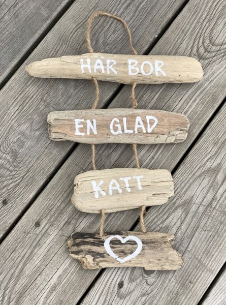 Vacker skylt i hängande drivved. Med text på drivvedsbitarna som sitter ihop med snören. Finns i två modeller/texter. -Här bor e