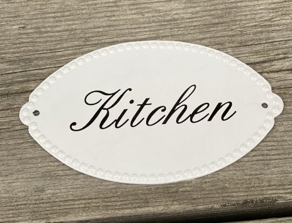Gammeldags skylt i emalj med text Kitchen i svart på vit botten. dekorerad med en pärl kant runt om. Skylten är oval i modell. N