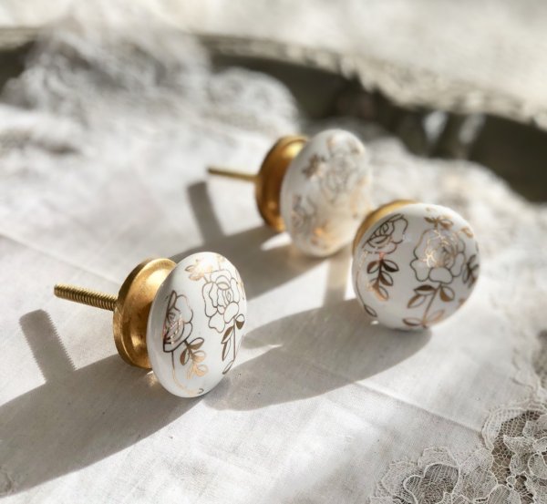 Vit porslins knopp i rundad halv platt modell. Dekorerad med rosor i guld samt krage och stomme i guld färgad metall. Längd: ca