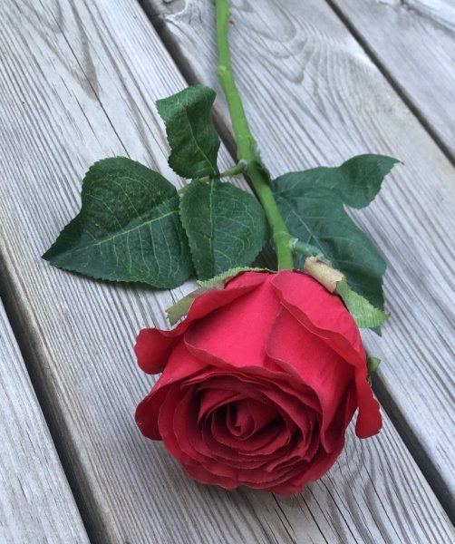 Vacker röd ros med gröna blad. Välarbetad vacker konstgjord ros med hög verklighets trogen känsla. Lika vacker ensam som i en bu