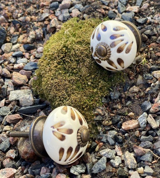 Rundad porslinsknopp med handmålat mönster i brunt, guld och vitt. Går i en orientalisk stil med utanpå liggande mönster. Välar