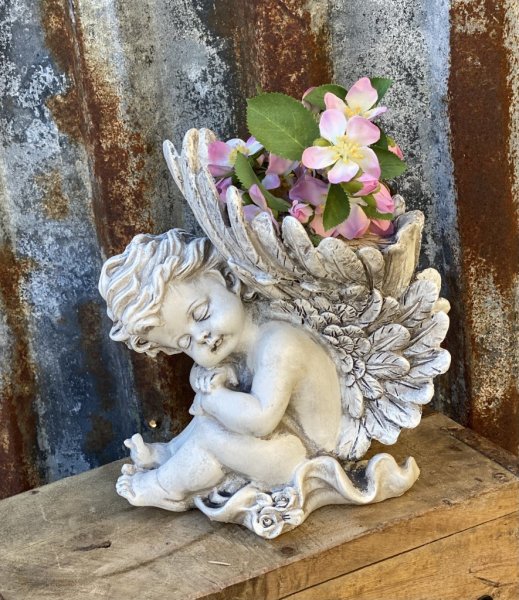 Vacker grå ängel som sitter ner och har stora vingar. På toppen av vingarna är det en avsats där man kan ställa ett ljus eller e