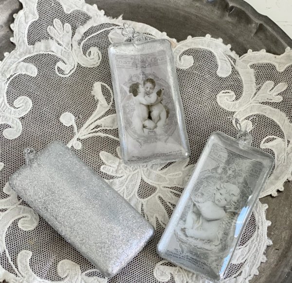 Julgranskula / dekorationskula i avlång modell med ängelmotiv. Finns i tre olika motiv -Pussande änglar -Ängel med blomsterkrans