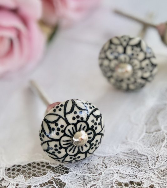 Rundad vit lätt Cream vit porslins knopp med svart blommönster runt om. Silverfärgad metall stomme. I och med en orientalisk kän