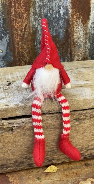 Söt tomte i tyg. I sittande modell med långa ben, passande att sitta på en kant och dingla med benen. Röd luva som halkat ner öv