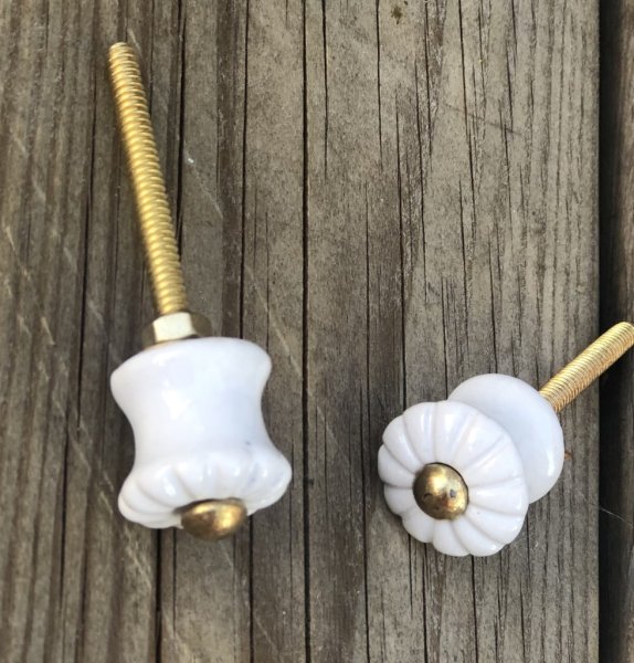 Vit keramik knopp av mindre modell detaljfullt dekorerad framtill med svaga veck och markerande mitt i guld. Längd: ca 7,5cm B