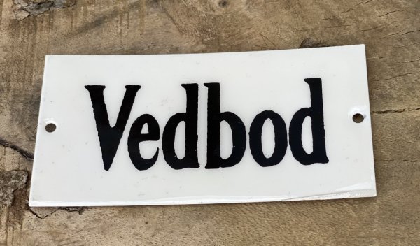 Gammeldags designad skylt Vedbod i plåt. Vit med svart text. I lätt ruffig stil.  Höjd: 4,5cm Längd: 9cm