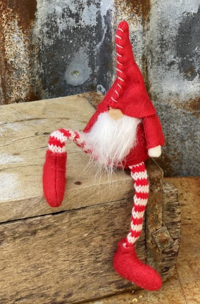 Söt tomte i tyg. I sittande modell med långa ben, passande att sitta på en kant och dingla med benen. Röd luva som halkat ner öv