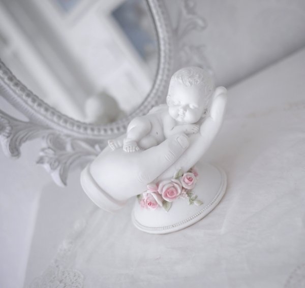 Vit ängel bebis som ligger i en öppen hand dekorerad med rosa rosor. En detalj full och välarbetad prydnad och minnes sak passan