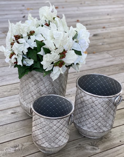 Tunna/kruka/urna i större modell med ledade handtag på sidorna. Lätt mönstrad och rundad i modellen, tillverkad i metall och går