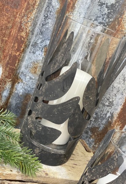 Ljuslykta blad i metall med cylinderglas inuti. Bladen går runt ljuslyktan och går i en svart ruffig nyans . Finns i två storle