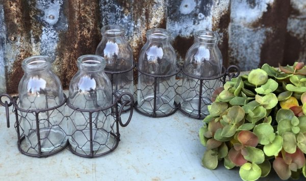 Glas vaser / flaskor som står i en nätad rost brun korg med ring formade handtag. Finns om två modeller -Två flaskor -Tre flasko
