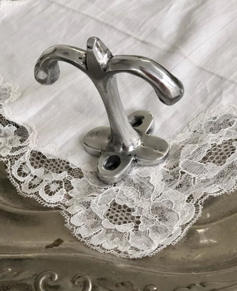 Silver färgad metall krok i dubbel modell. Med blomformad rygg platta som fästes i tex hyllan eller takets undersida så kroken