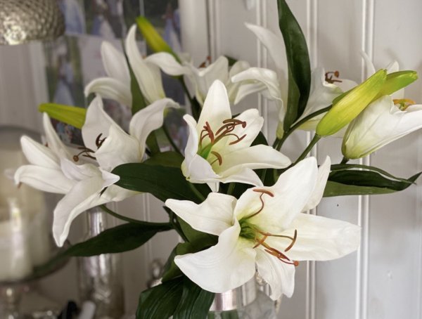 Vacker vit lilja i högre/längre modell med utslagen blomma och knopp samt flera gröna blad. Välarbetad och verklighetstrogen kon