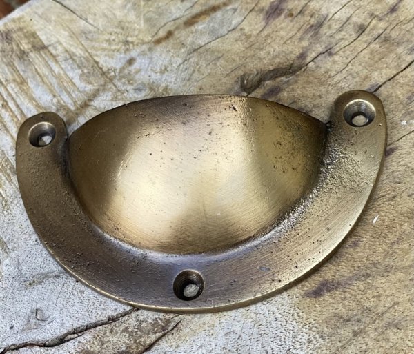 Skålformat handtag i metall. Går i en guld färgad nyans. Handtaget kan sättas med öppningen uppåt och nedåt. Mäter 9,5*5,5*2cm